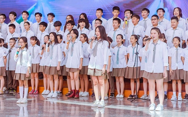 Hình ảnh tập thể học sinh mặc đồng phục áo trắng biểu diễn trên sân khấu, minh họa trực quan cho nhu cầu giữ gìn sự chỉn chu của trang phục đầu tuần.
